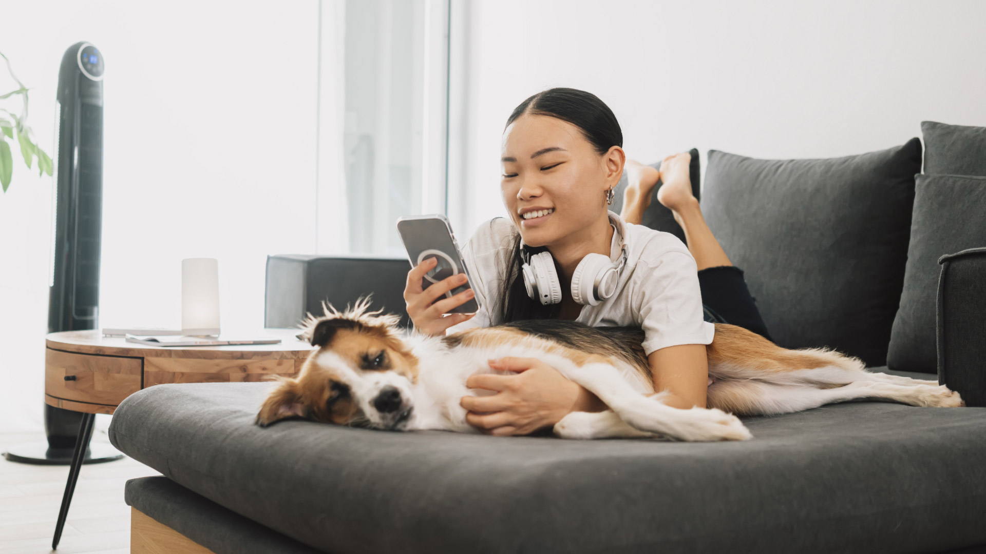 A woman on her phone lounges on a couch with her dog