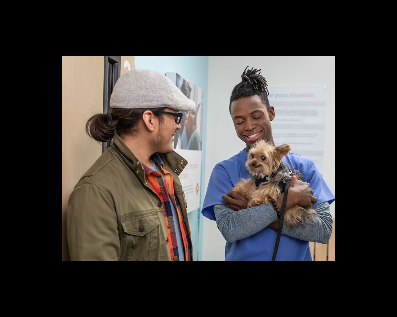 A dog owner looking at his happy little dog held by a young male veterinarian at the Banfield Pet Hospital