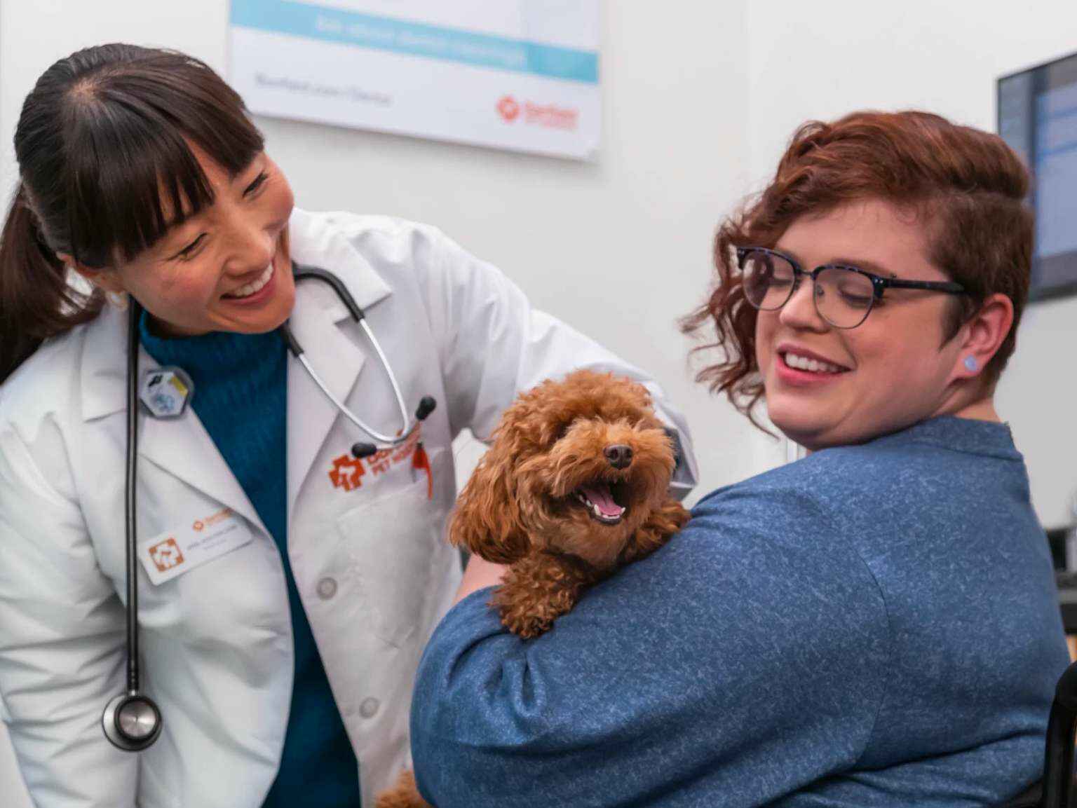 A dog owner holding her Toy Poodle puppy in her arms and talking to a young female veterinarian at the Banfield Pet Hospital