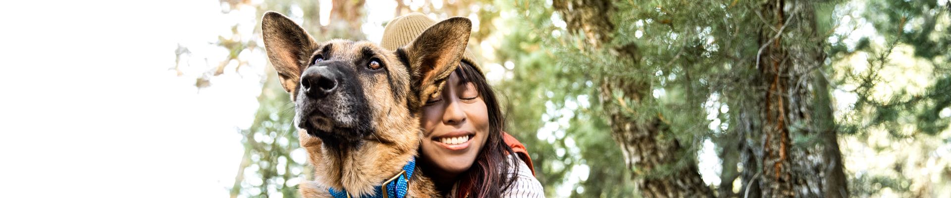 smiling woman hugs dog under trees
